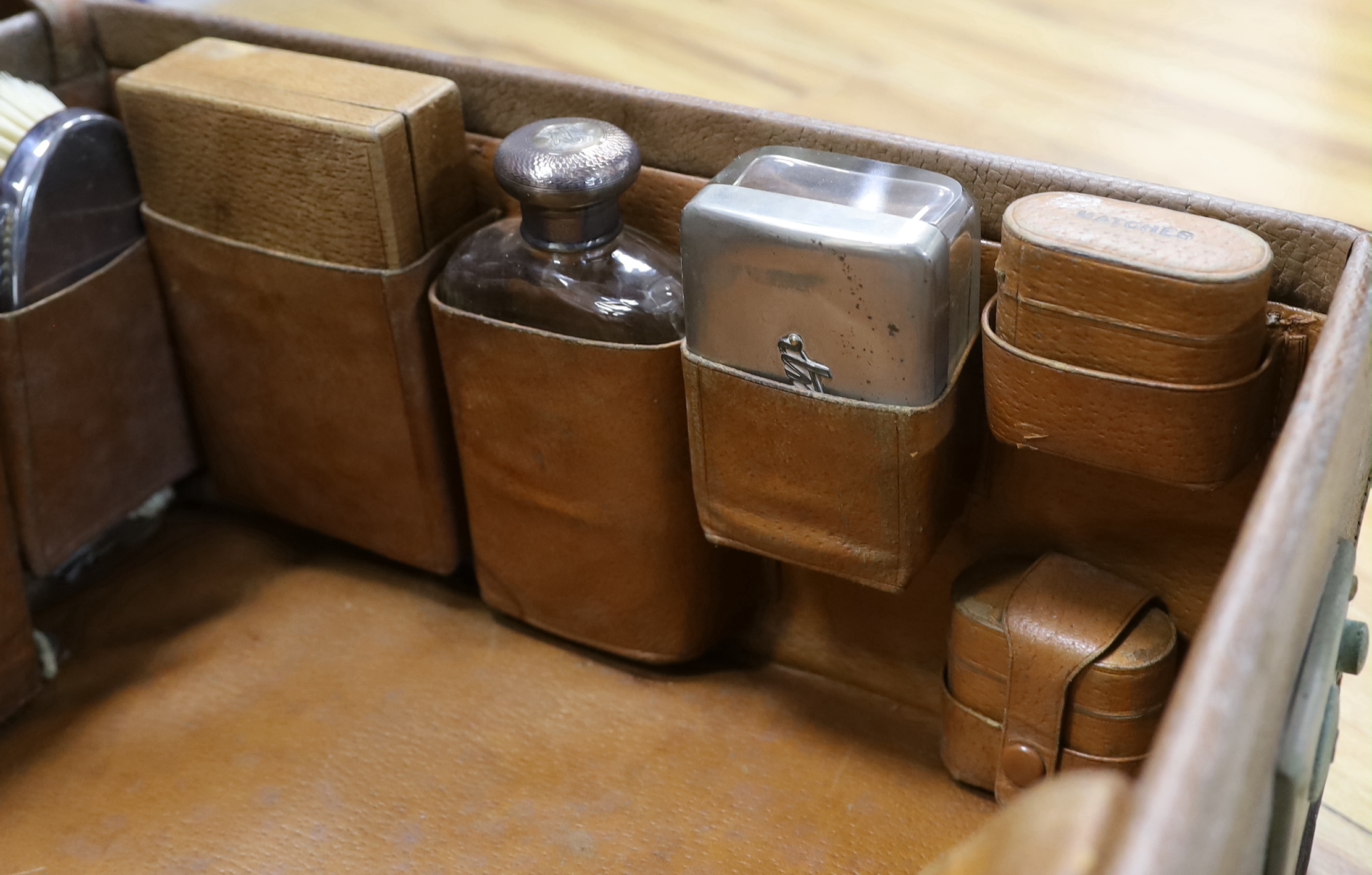 An Edwardian leather travelling toilet case, containing eleven silver mounted toilet jars etc. including a mounted glass hip flask and easel mirror, Drew & Sons, London, 1905, case width 62.5cm.